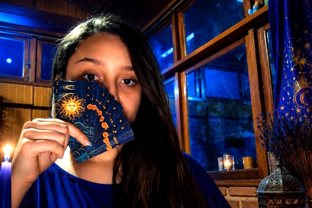 Mãe Dary segurando cartas de tarô em um ambiente místico iluminado por velas